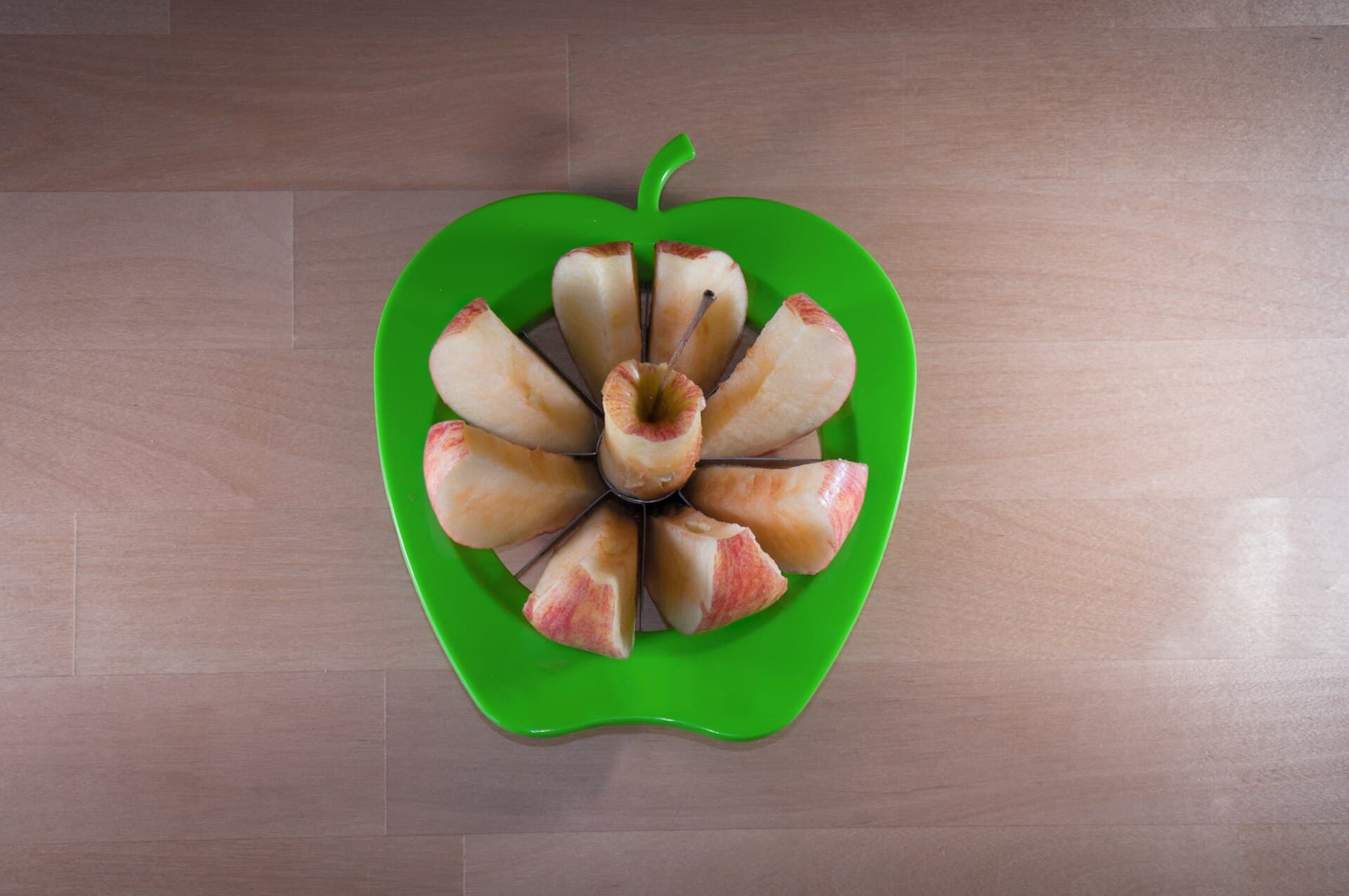 Ein Apfel, mit einem Apfelteiler in Schnitze geschnitten, liegt auf einem Holztisch