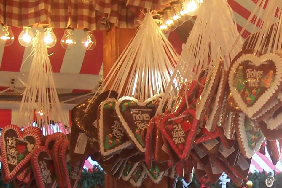 Lebkuchenherzen mit „Frohes Fest“ und „Ich liebe Dich“ hängen an weißen Bändern an einem Weihnachtsmarktstand mit rot-weißem Dach