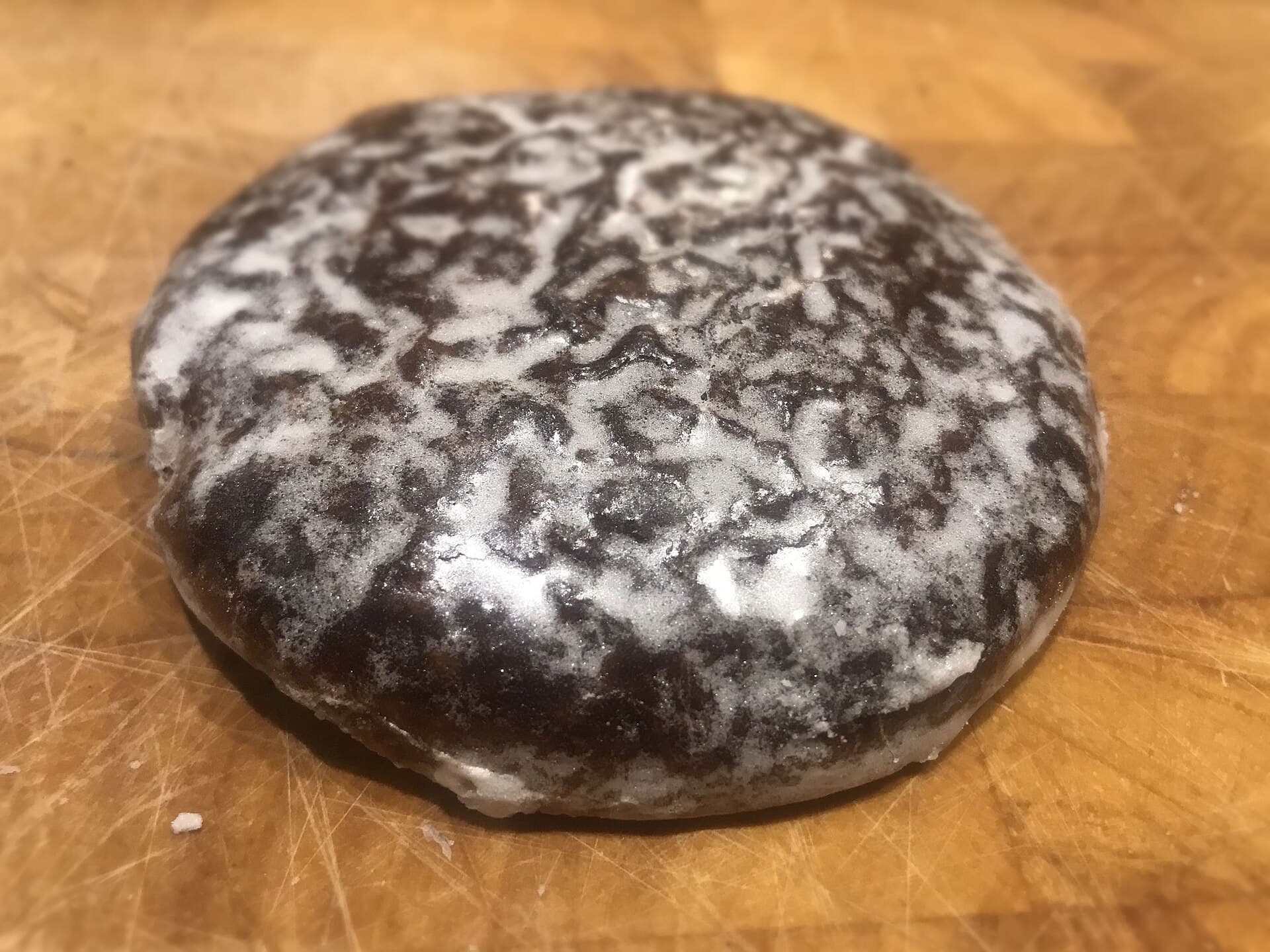 Ein einzelner dunkler Nürnberger Lebkuchen mit weißer, marmorierter Zuckerglasur auf einem Holzbrett