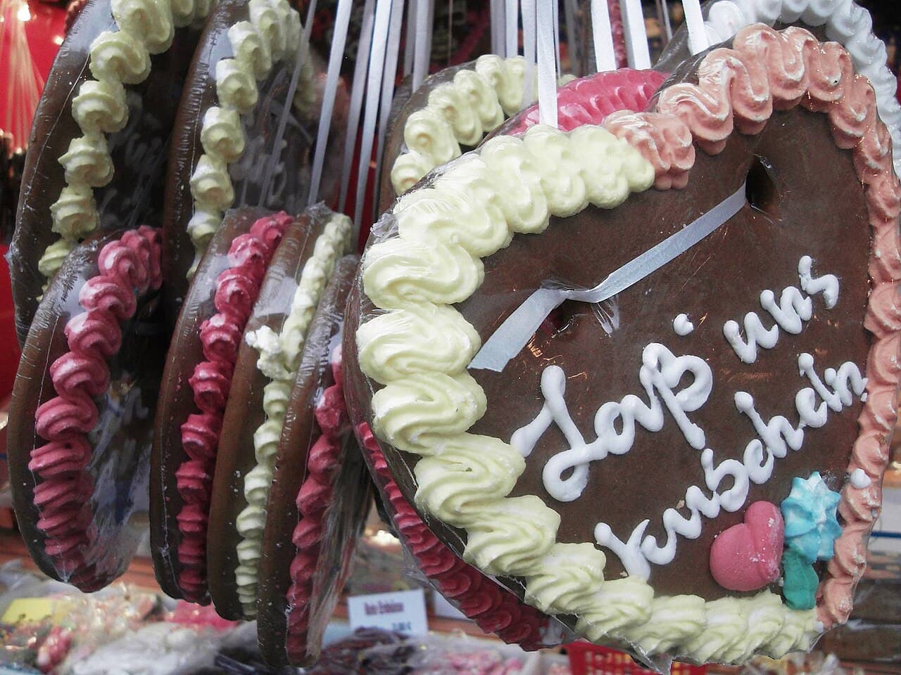 Nahaufnahme eines Lebkuchenherzes mit dickem Rand aus Zuckerguss-Tupfen in Gelb und Rosa und weißer Zuckerschrift